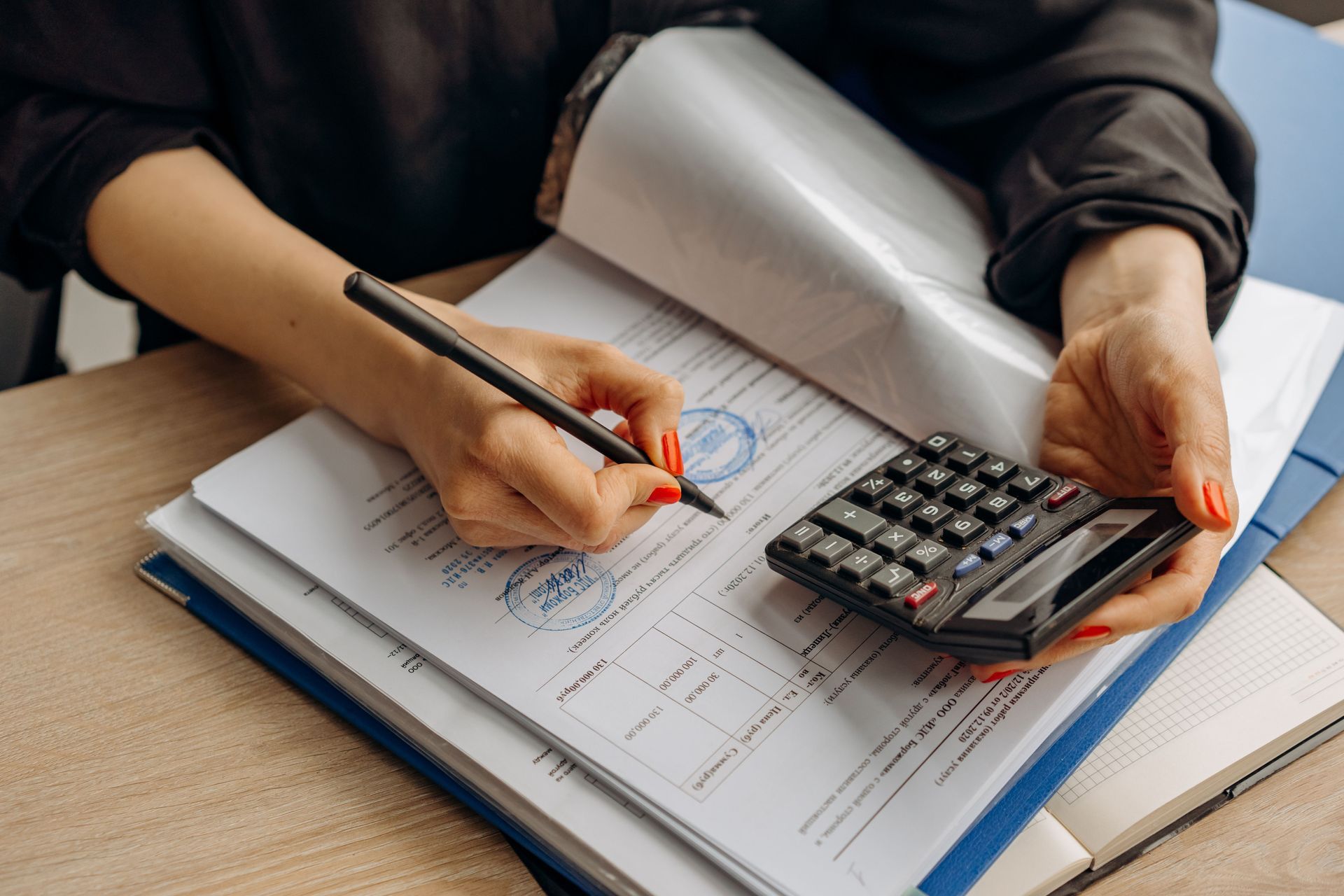 Une personne remplit un formulaire à côté d'une calculatrice et d'un bloc-notes posés sur un bureau.
