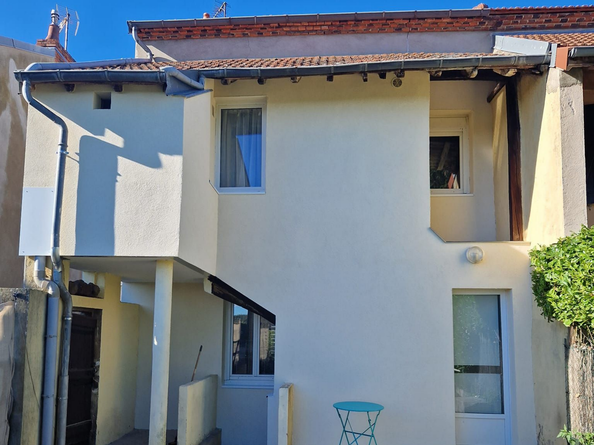 Une maison de deux étages couleur crème avec un petit balcon, un escalier extérieur et une petite table sur la terrasse.