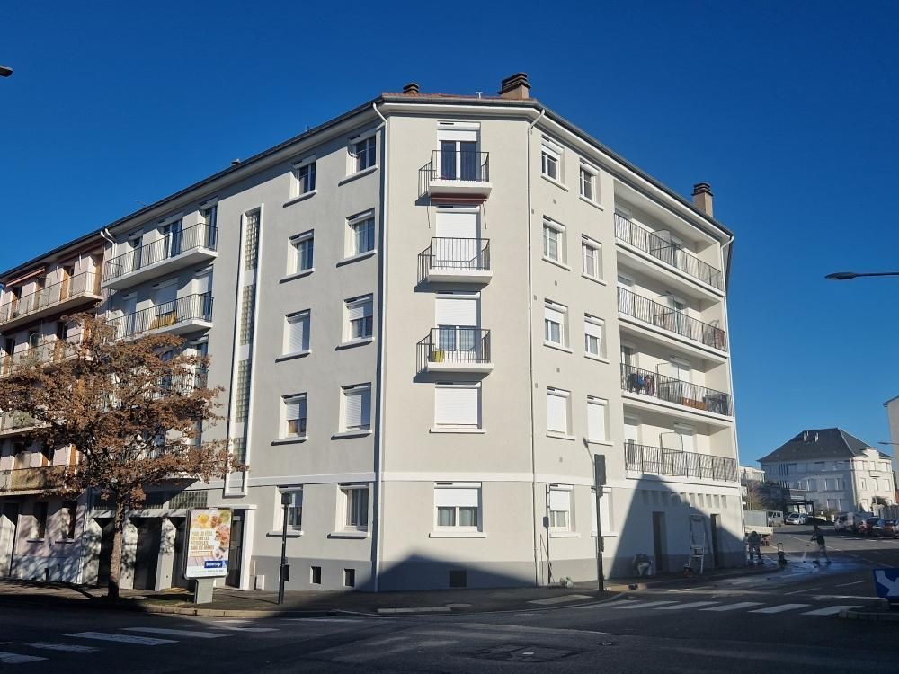 Un immeuble d'appartements clair à plusieurs étages, situé à un coin de rue sous un ciel bleu limpide.