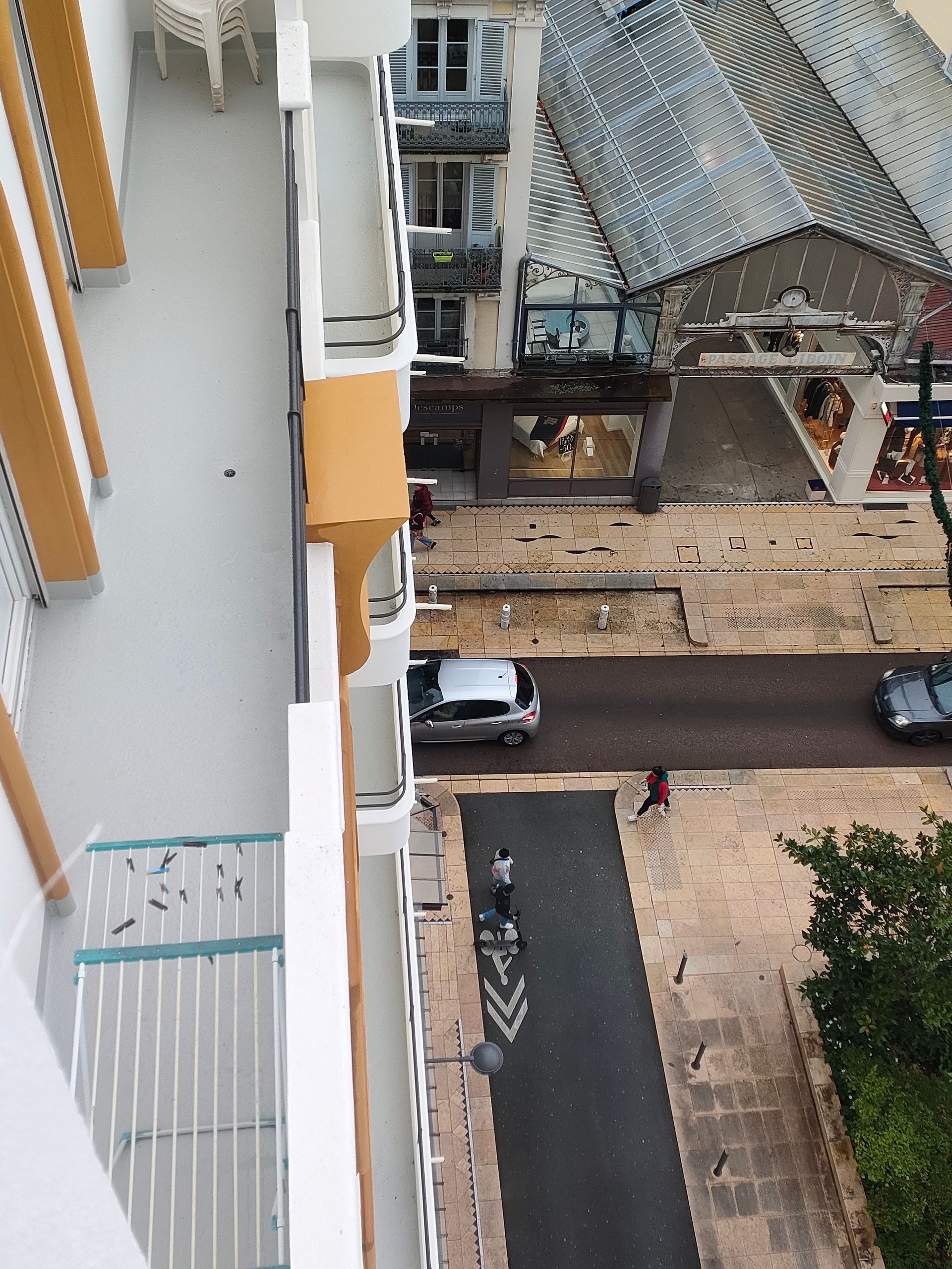 Vue en plongée d'un balcon d'appartement blanc avec un étendoir à linge donnant sur une rue avec des voitures et la façade d'un immeuble.