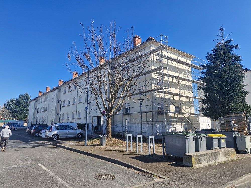 Un immeuble d'appartements de plusieurs étages en rénovation, avec des échafaudages sur un côté, situé en zone urbaine sous un ciel dégagé.