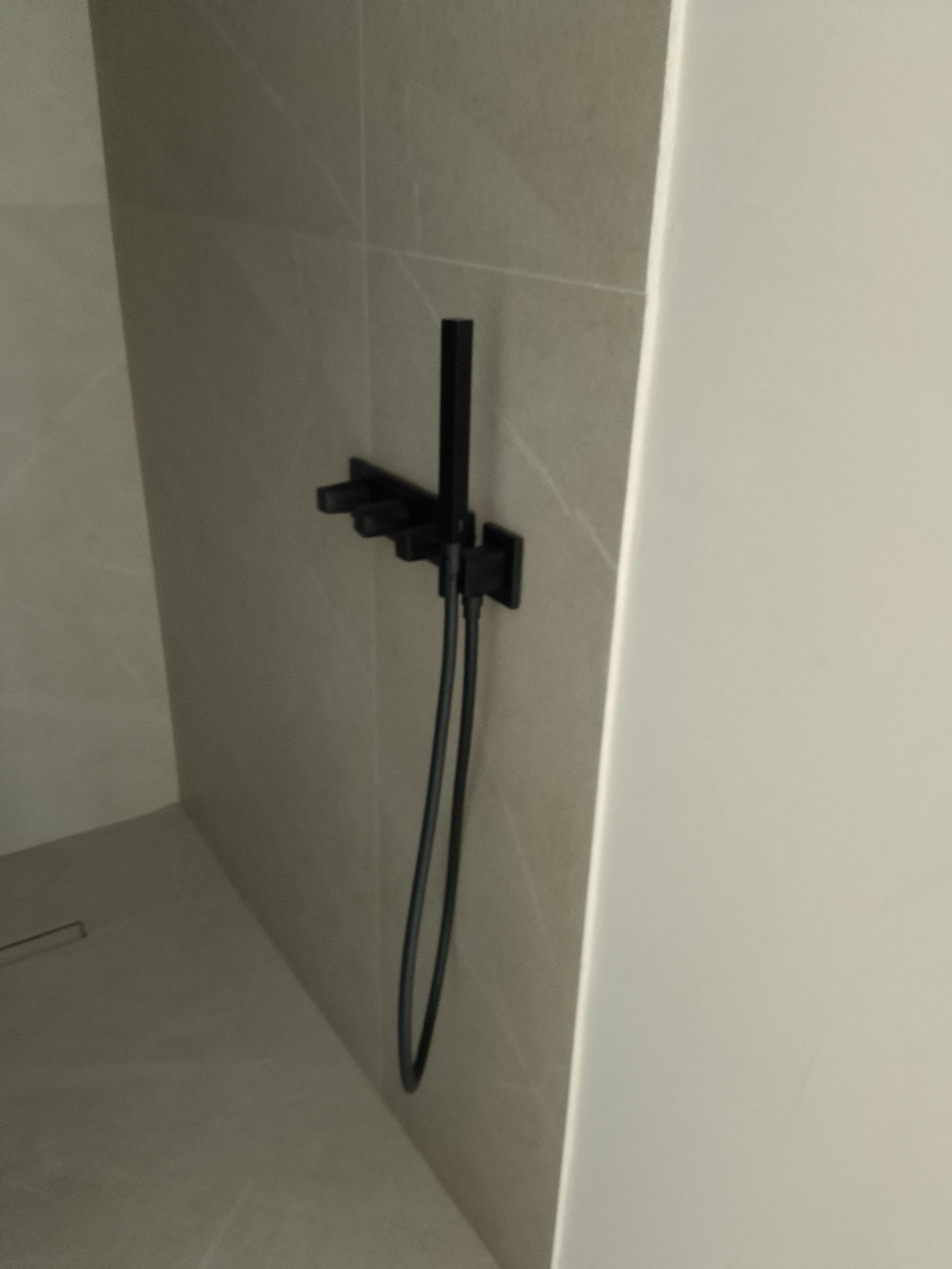 Accesorio de ducha de color negro sobre una pared de azulejos de color gris claro en una cabina de ducha.