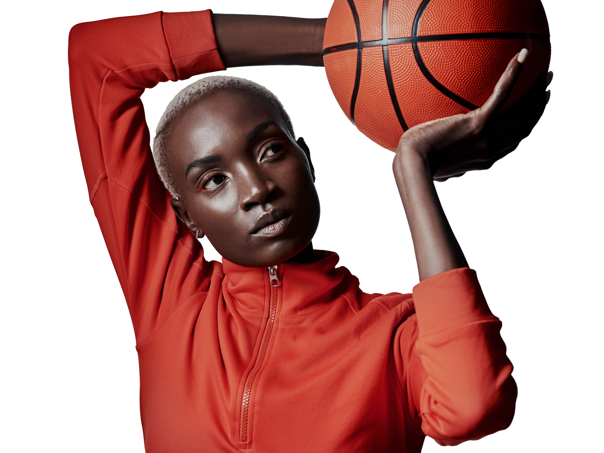 Frau in orangefarbenem Oberteil hält einen Basketball und schaut in die Kamera. Beigefarbener Hintergrund.