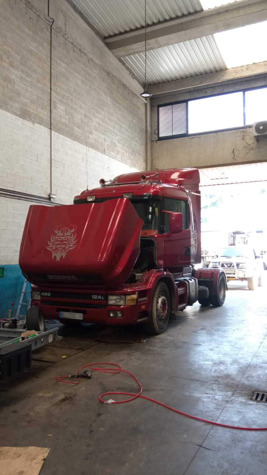 Un camión semirremolque rojo está estacionado en un garaje con el capó abierto.