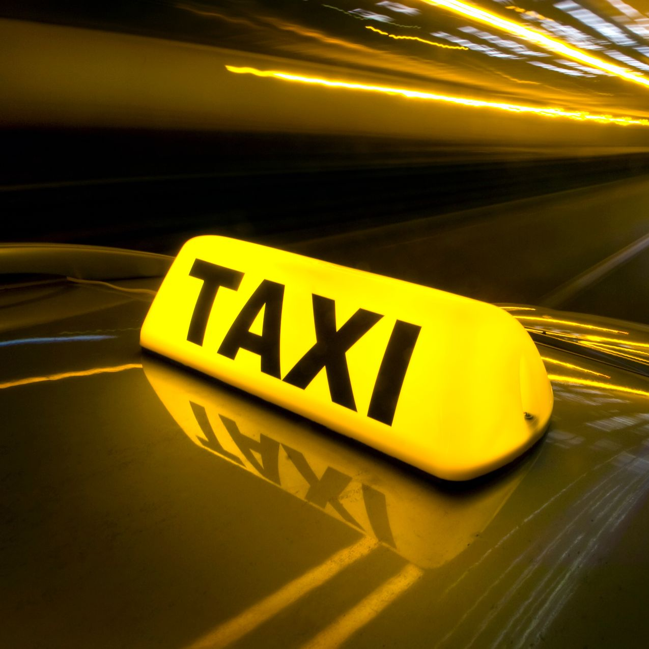 Un gyrophare jaune vif de taxi avec l'inscription TAXI sur le toit d'une voiture sombre aux feux flous.