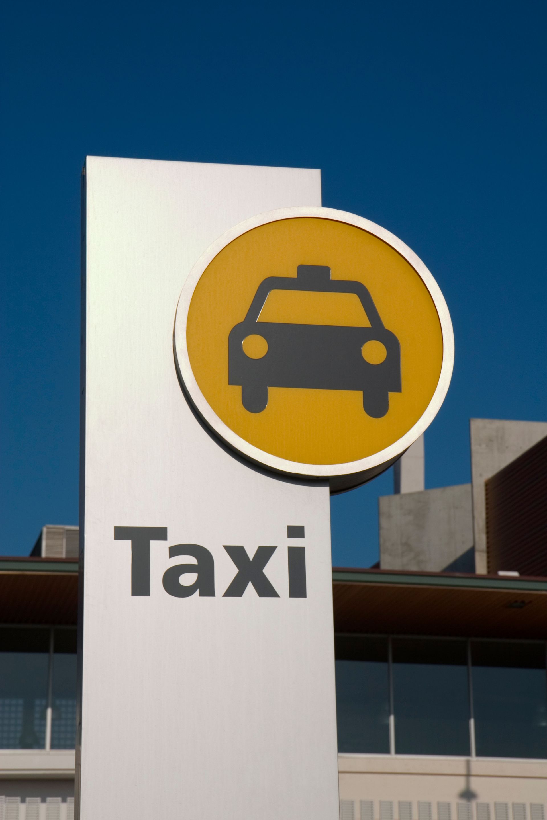 Panneau de taxi avec un cercle jaune orné d'une icône de taxi noire ; poteau blanc avec l'inscription Taxi.