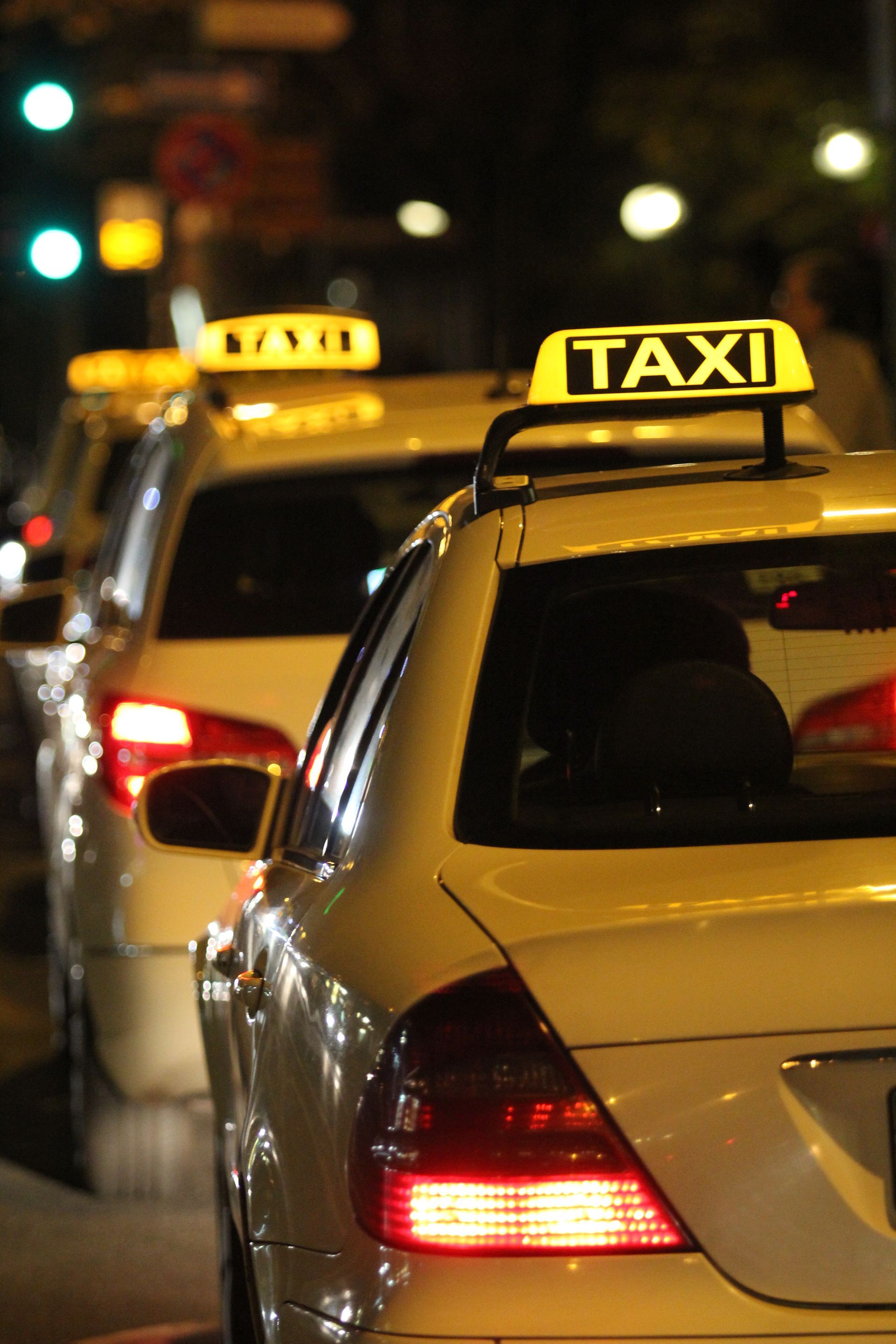 Des taxis alignés dans une rue de la ville la nuit, panneaux lumineux, taxis jaunes avec feux arrière rouges.