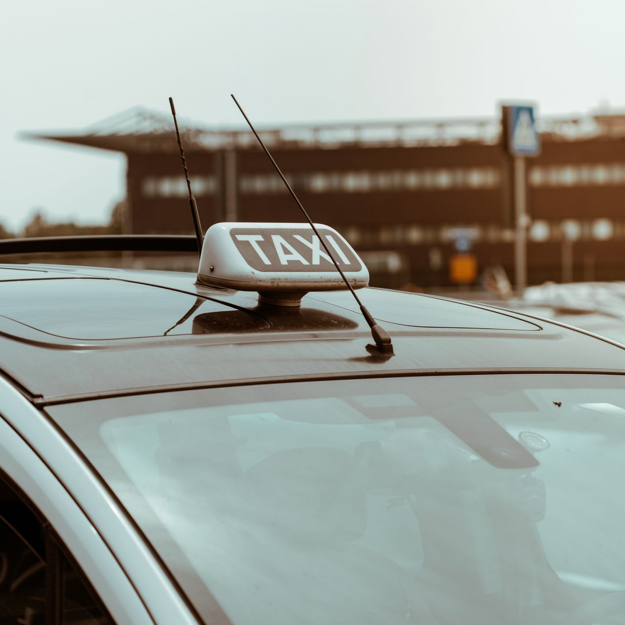 Toit d'un taxi avec panneau TAXI et antennes, stationné devant un bâtiment.