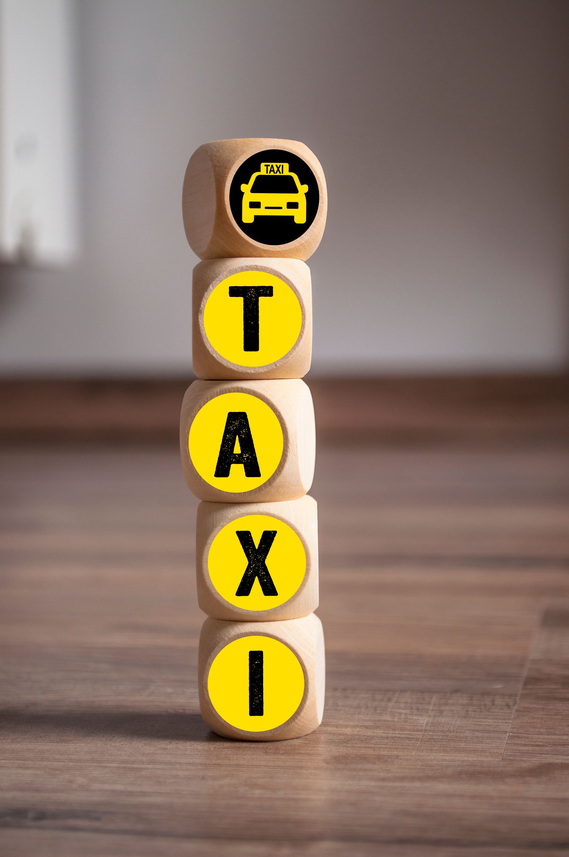 Des dés en bois empilés pour former le mot TAXI, avec un symbole de taxi sur le dessus.