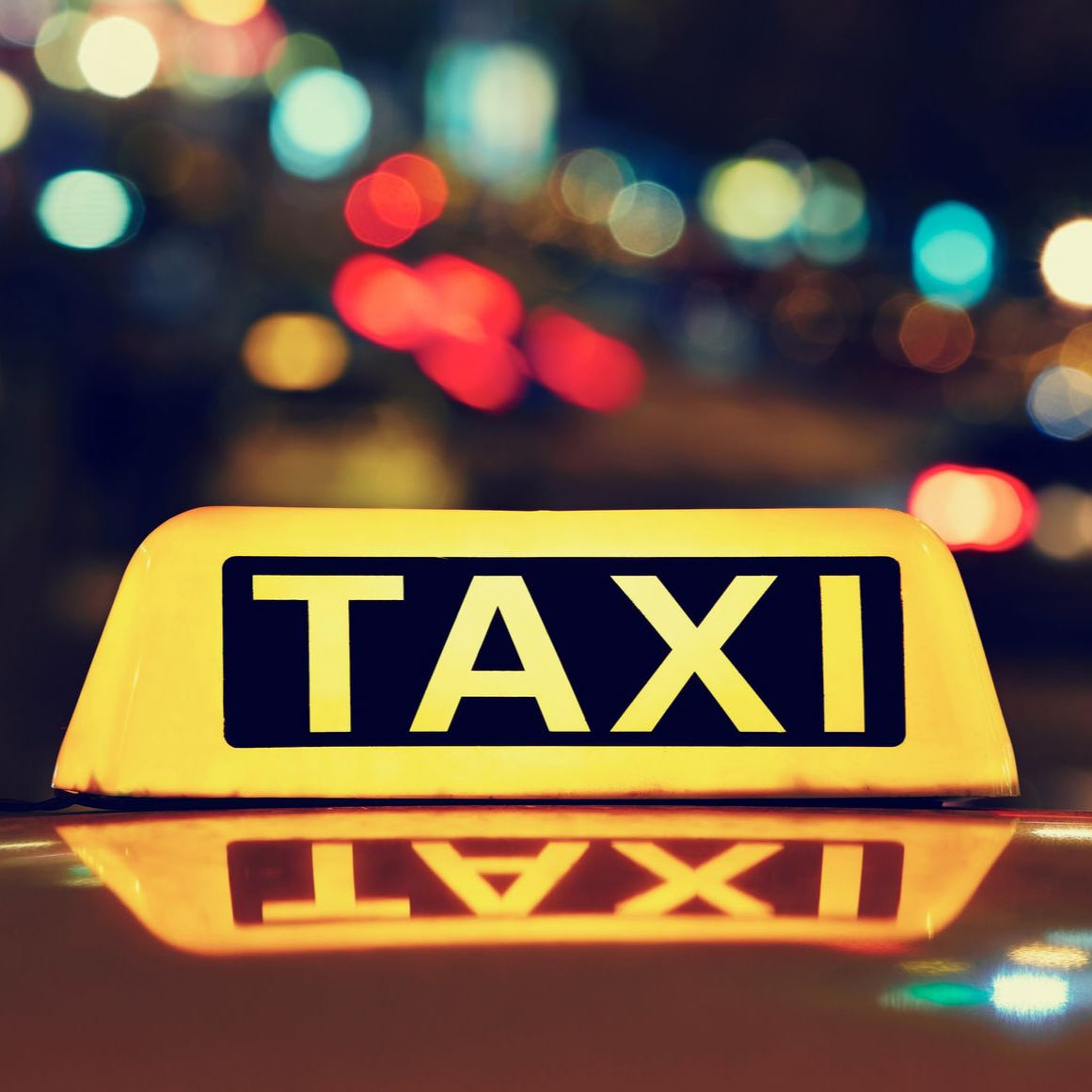 Panneau jaune de taxi avec l'inscription TAXI illuminé sur un fond de nuit urbaine floue.