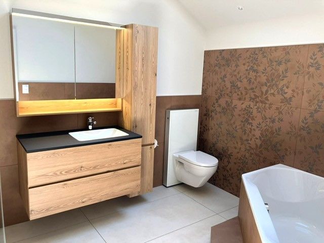 Badezimmer mit Waschtisch, Toilette und Badewanne aus Holz. Braune Akzentwand.