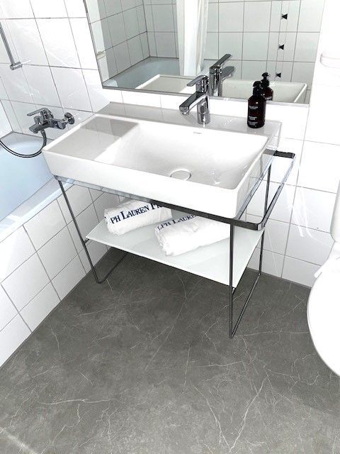 Steinwaschbecken auf Holzplatte, Chromarmatur, schwarze Accessoires.