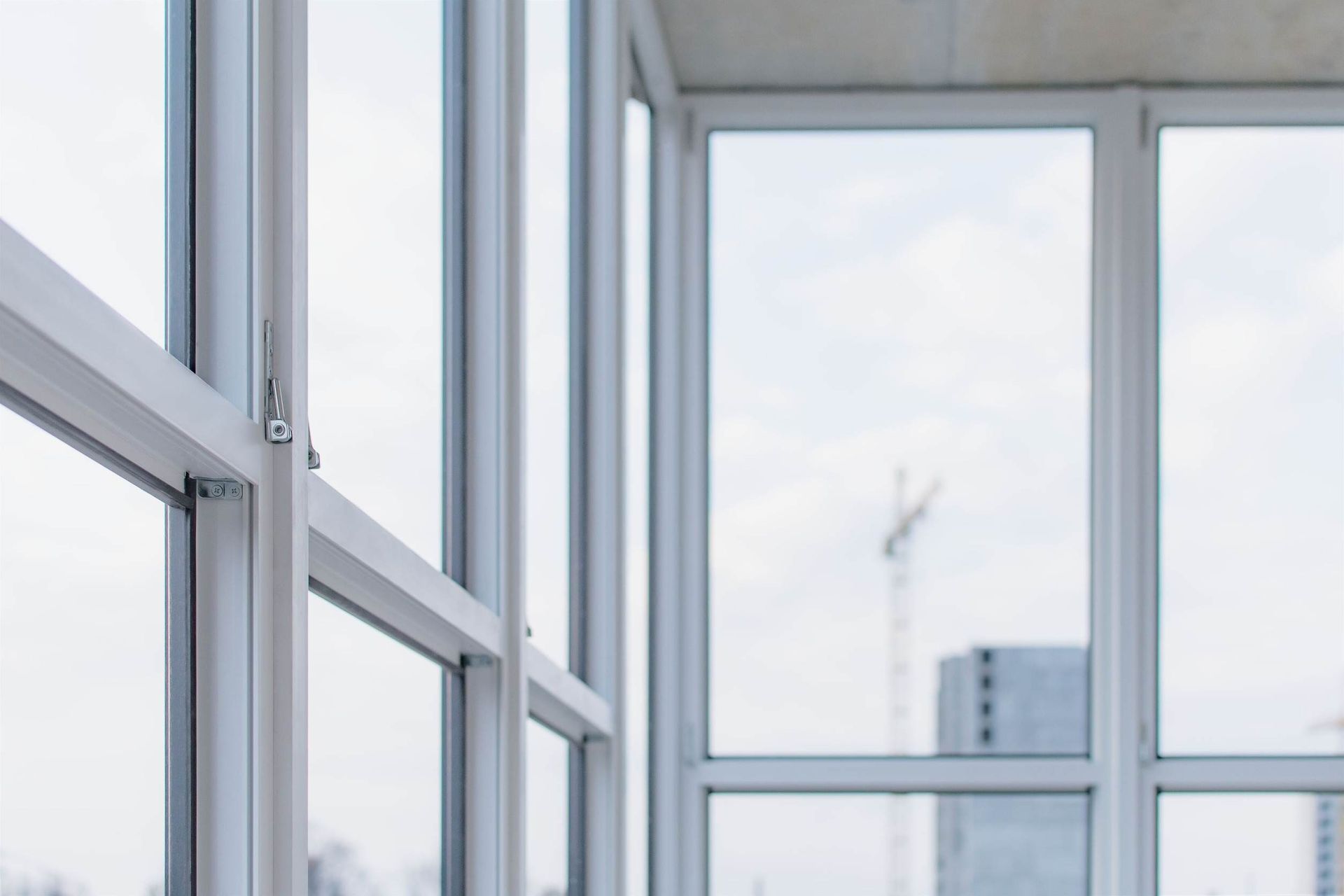 Ventanas de vidrio con marco blanco en el interior de una habitación luminosa, con un edificio parcialmente visible y una grúa de construcción en la distancia.
