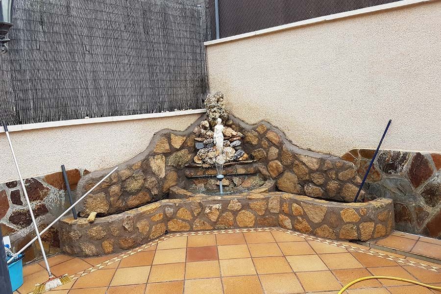 Fuente de piedra con fuente en un patio de baldosas. Colores marrón y tostado.