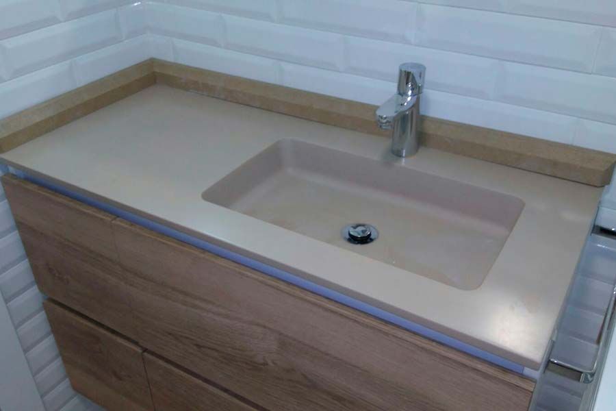 Mueble de baño con gabinetes de madera, encimera beige, lavabo integrado y grifería cromada.