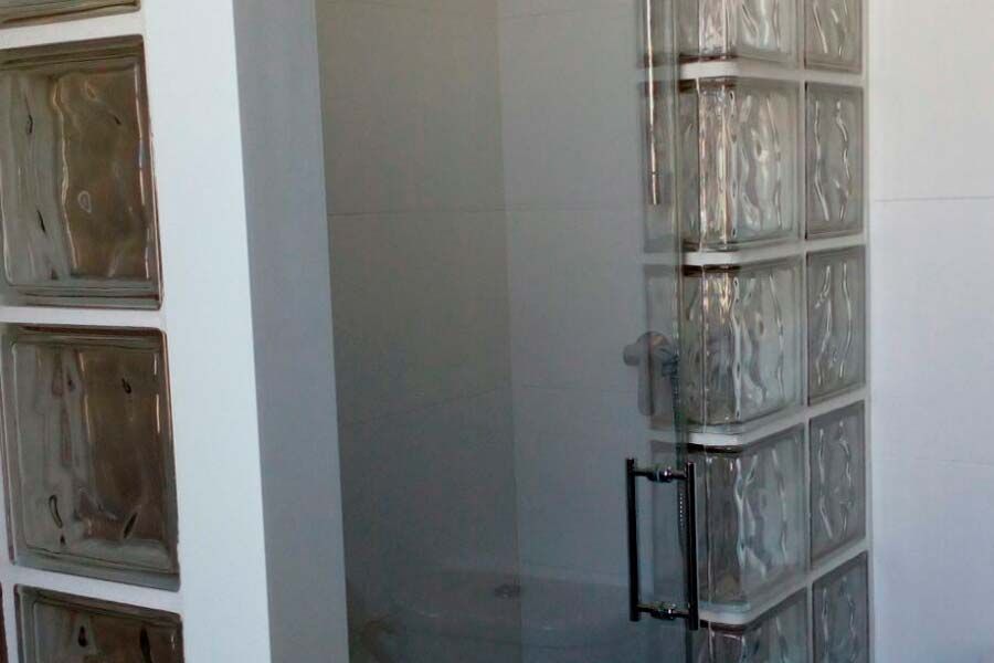 Mampara de ducha con pared de bloques de vidrio y puerta de cristal abatible.