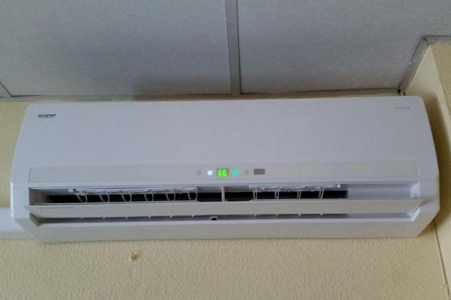 Unidad de aire acondicionado blanca montada en una pared beige, debajo de un techo blanco.