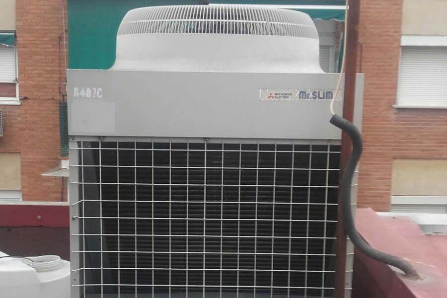 Unidad de aire acondicionado exterior con rejilla metálica y ventilador en cubierta.