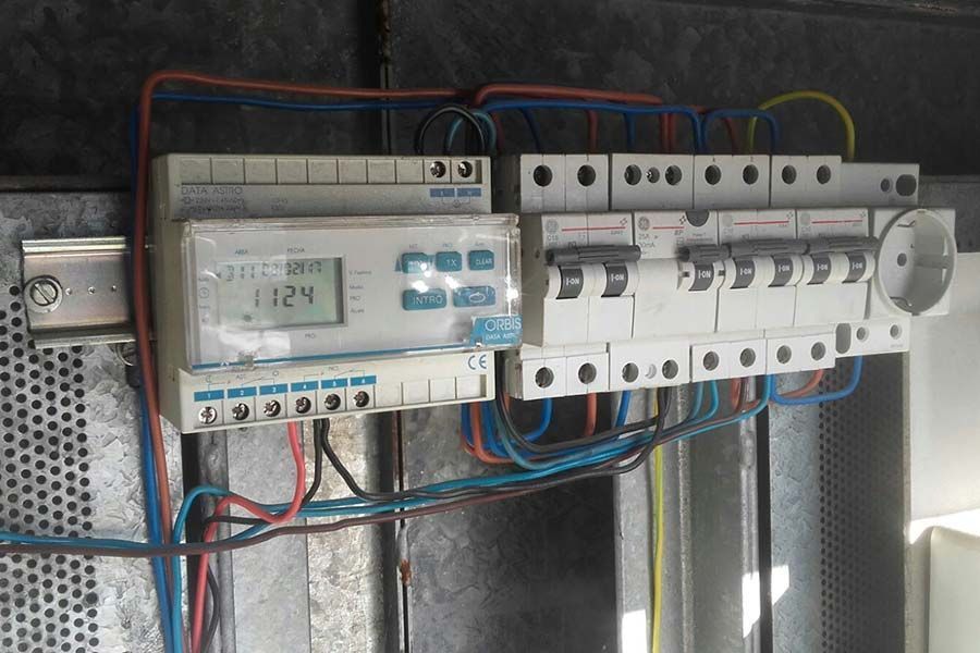 Panel eléctrico con temporizador, disyuntores y cableado contra una superficie metálica.