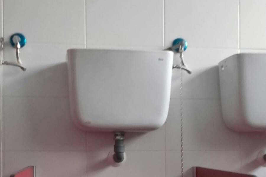 Tanque de inodoro de pared de color blanco, con grifo con manija azul y cadena.