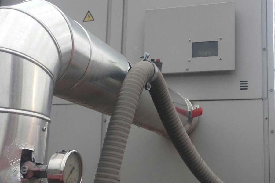 Tuberías metálicas aisladas y una manguera gris conectadas a una unidad industrial. Se ve un manómetro.