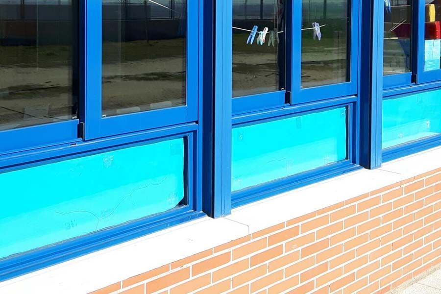 Marcos de ventanas azules con paneles cian, encima de una pared de ladrillos.