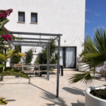 Une maison blanche avec une pergola et des plantes en pot devant.