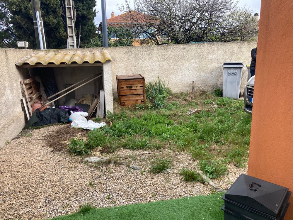 Une cour arrière avec un cabanon et une poubelle.