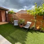 Une cour arrière avec une clôture en bois, des chaises et des plantes en pot.