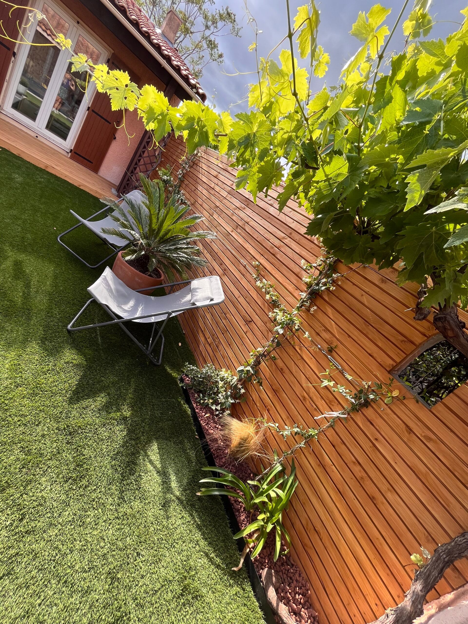 Une clôture en bois entoure une pelouse verte luxuriante devant une maison.