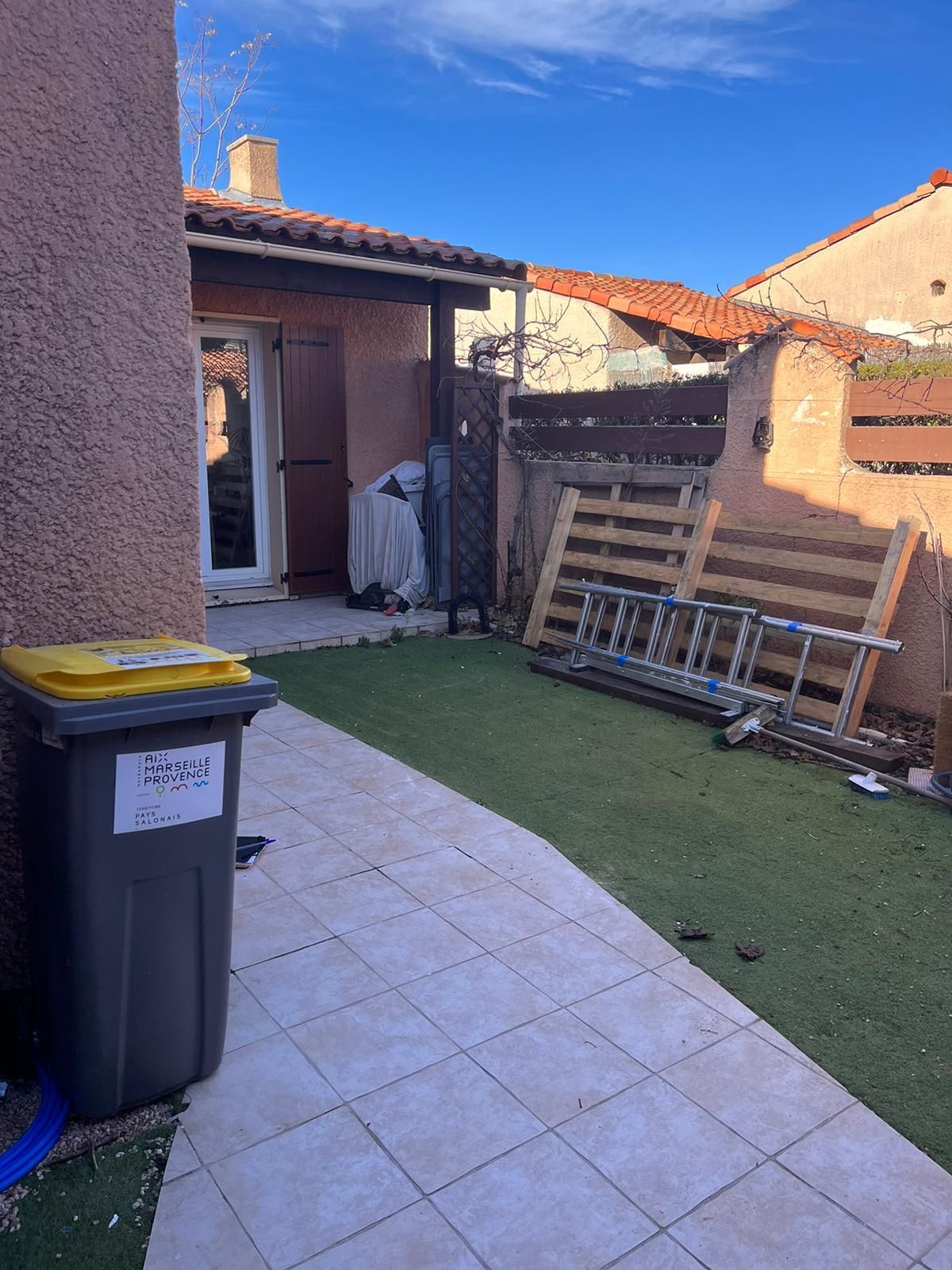 Une poubelle avec un couvercle jaune se trouve dans l'arrière-cour d'une maison.