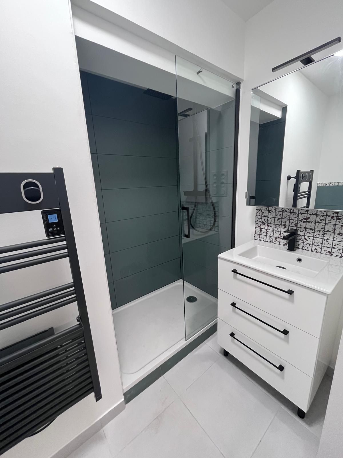 Une salle de bain avec lavabo, douche, miroir et porte-serviettes.