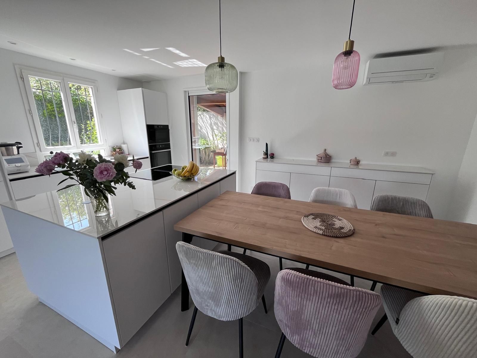 Une salle à manger avec une table et des chaises et une cuisine en arrière-plan.