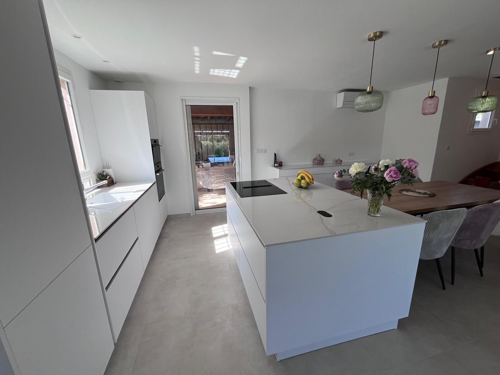 Une cuisine avec des armoires blanches, un grand îlot, une table et des chaises.