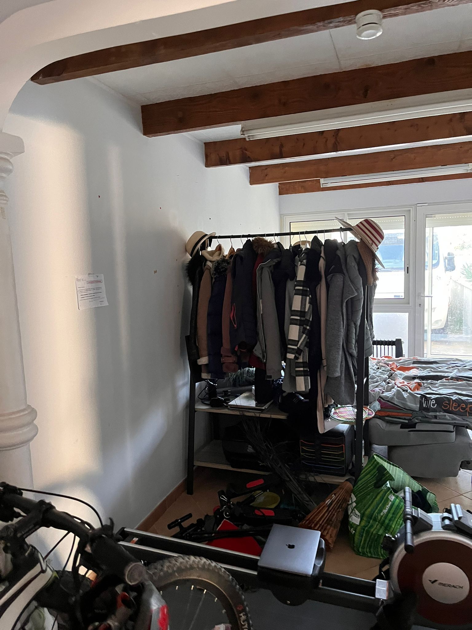 Une pièce en désordre avec un portant et un ordinateur portable sur le sol.