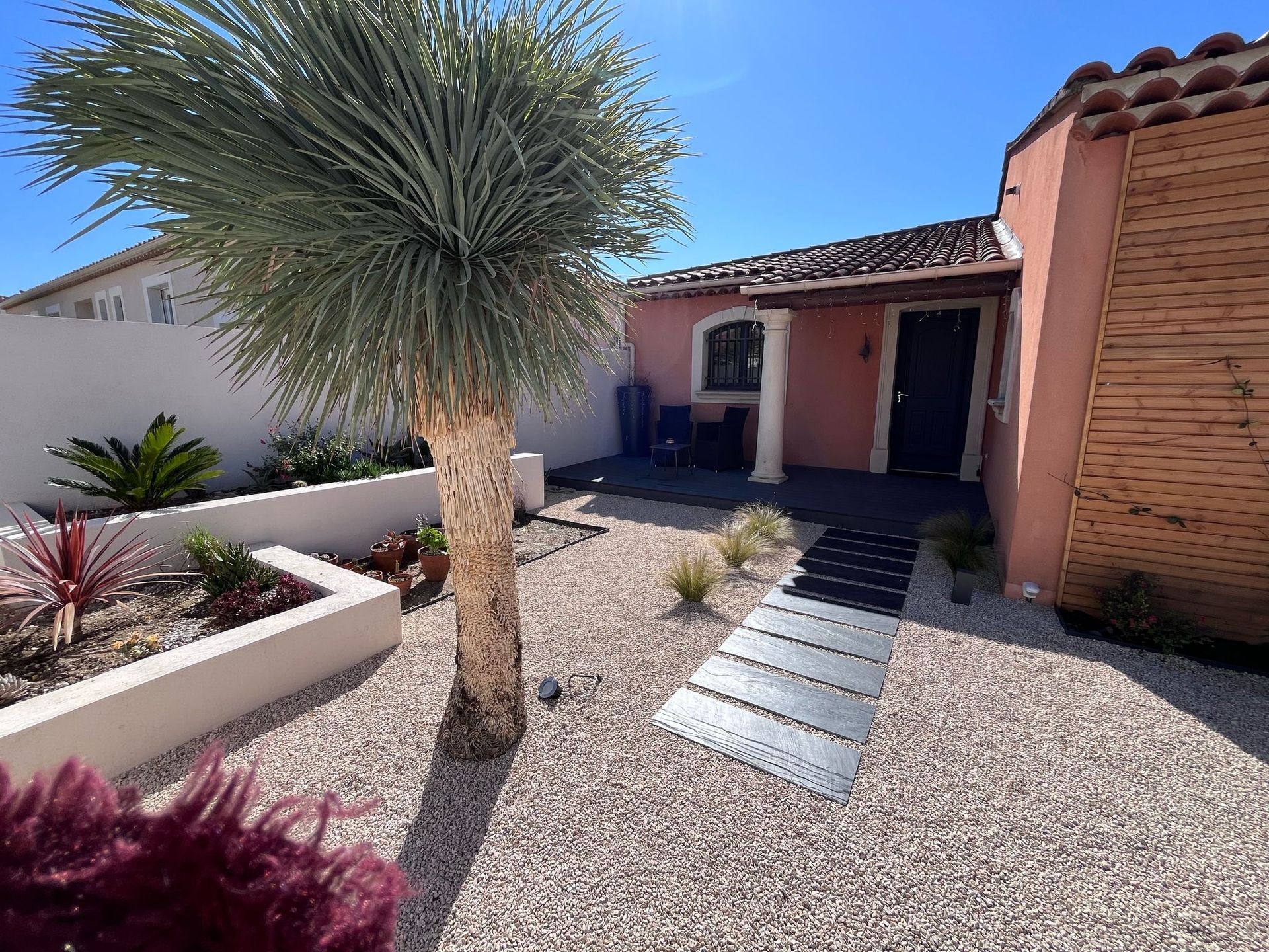 Une allée de gravier à côté d'un bâtiment orange avec des volets sombres.