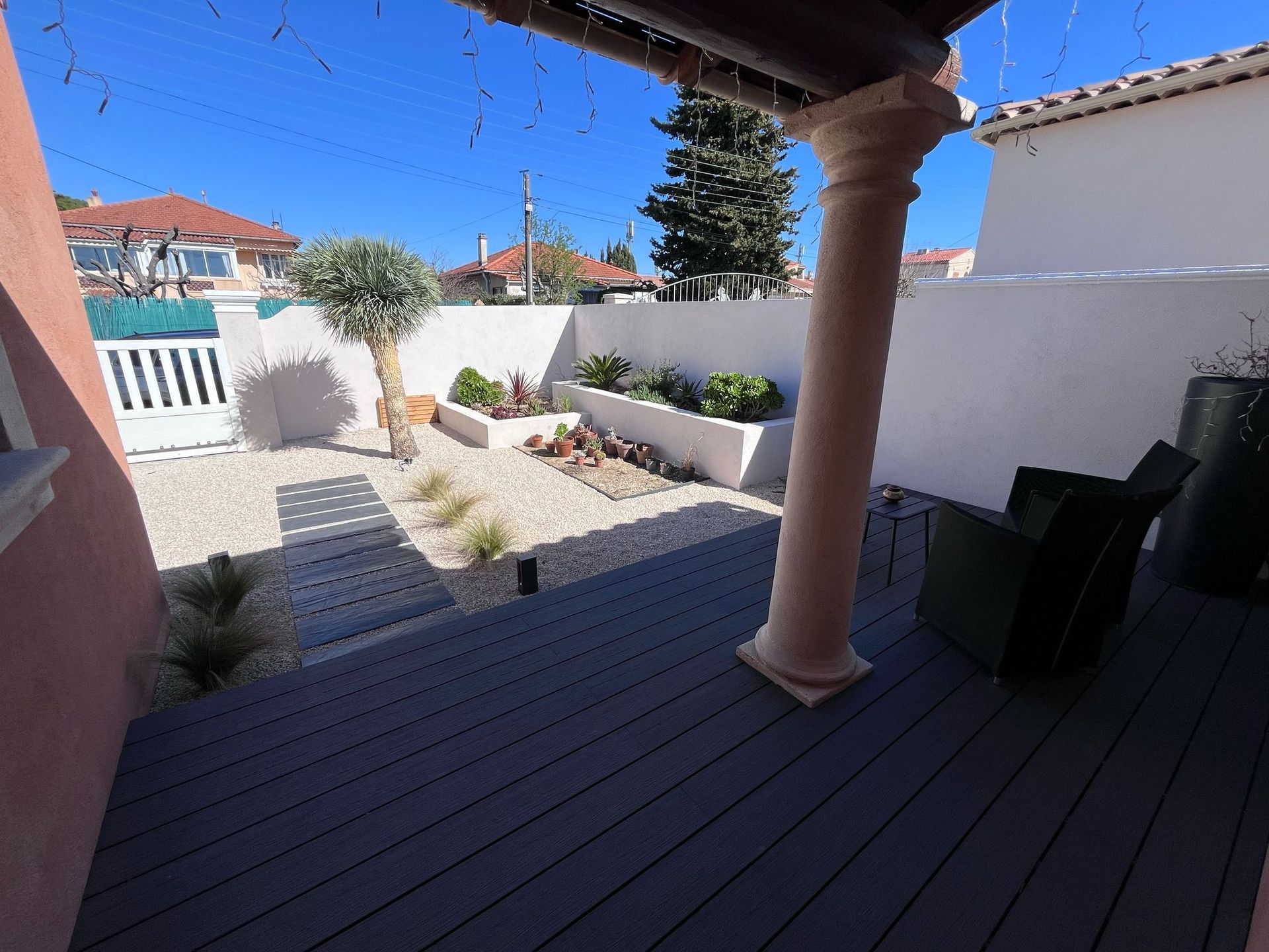 Patio arrière avec terrasse grise, jardin de gravier, murs blancs et colonne décorative.
