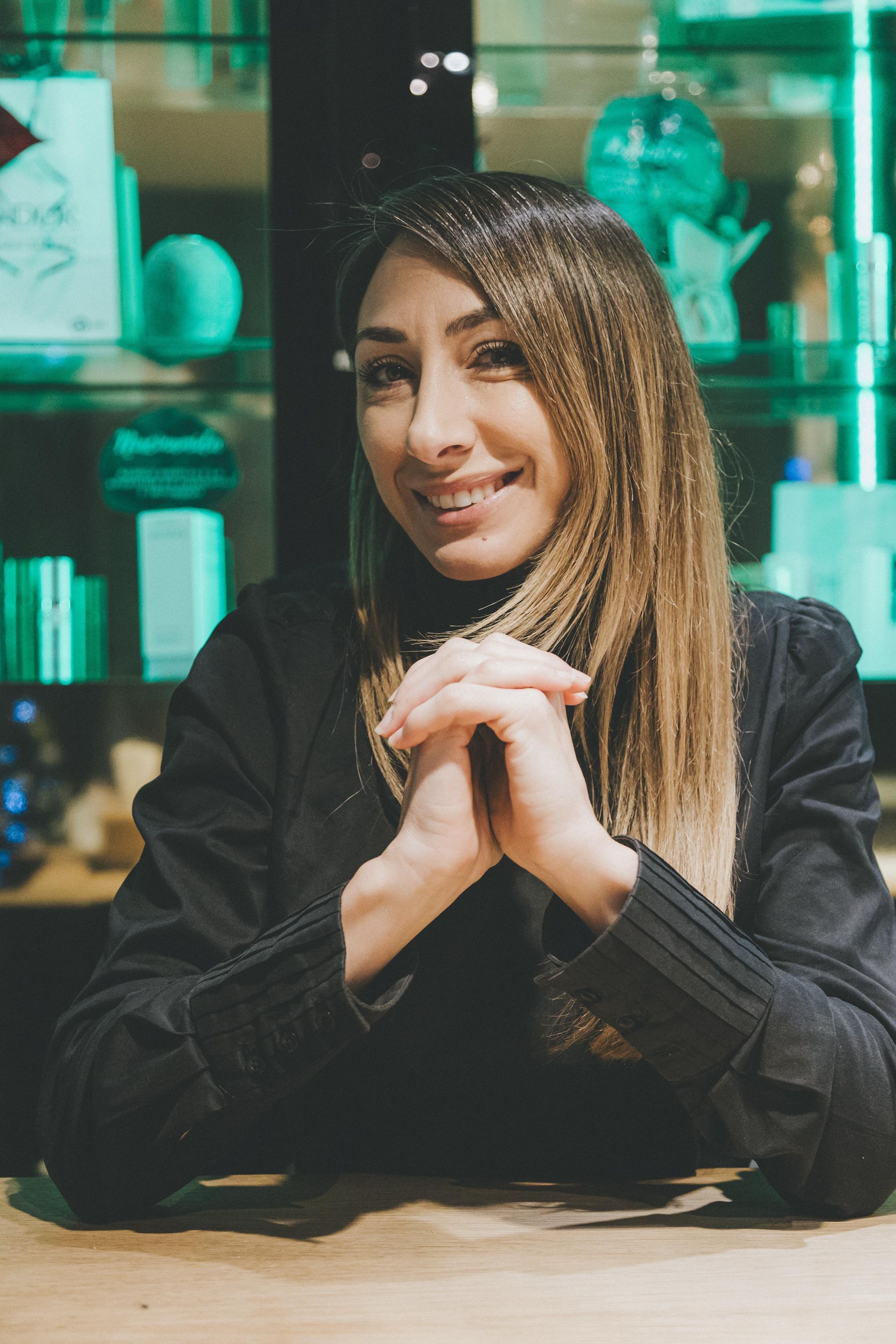 Una mujer está sentada en una mesa con las manos juntas y sonriendo.