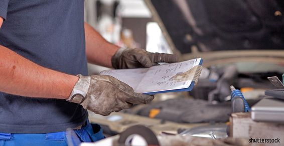 Un mécanicien, gants sales aux mains, tenant un bloc-notes, inspecte le moteur d'une voiture.