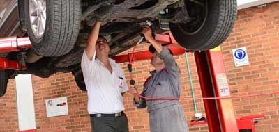 Deux mécaniciens travaillent sur une voiture soulevée par un pont élévateur dans un garage.