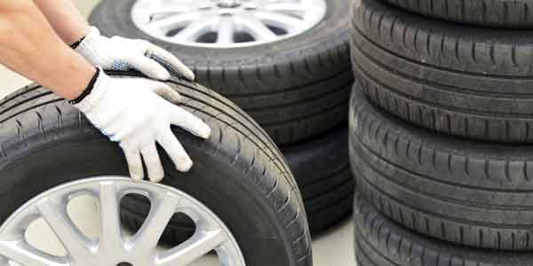 Des mains gantées manipulent un pneu de voiture, avec une pile de pneus en arrière-plan.