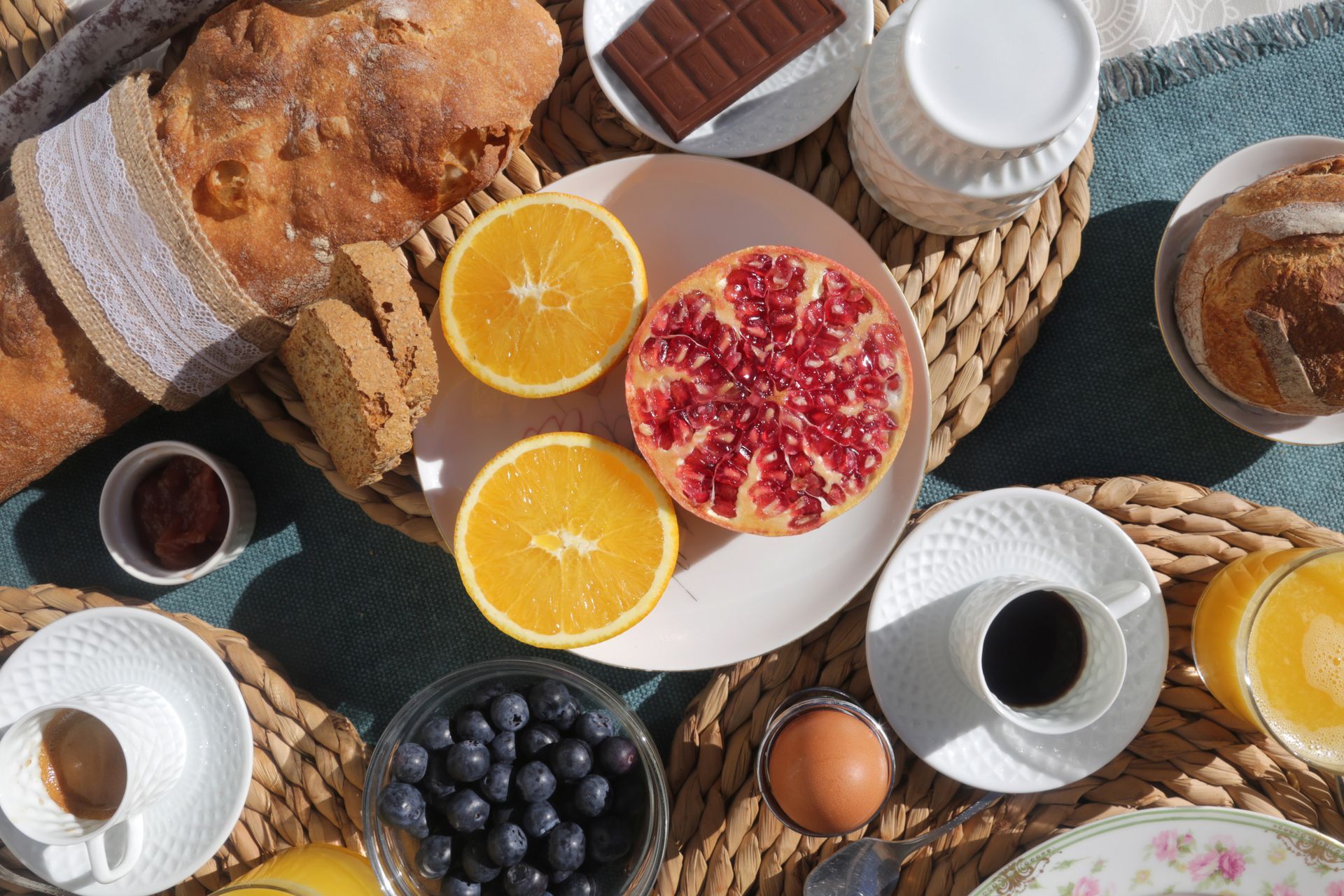 Desayuno compuesto por pan, fruta, café, chocolate y huevos sobre una estera tejida.