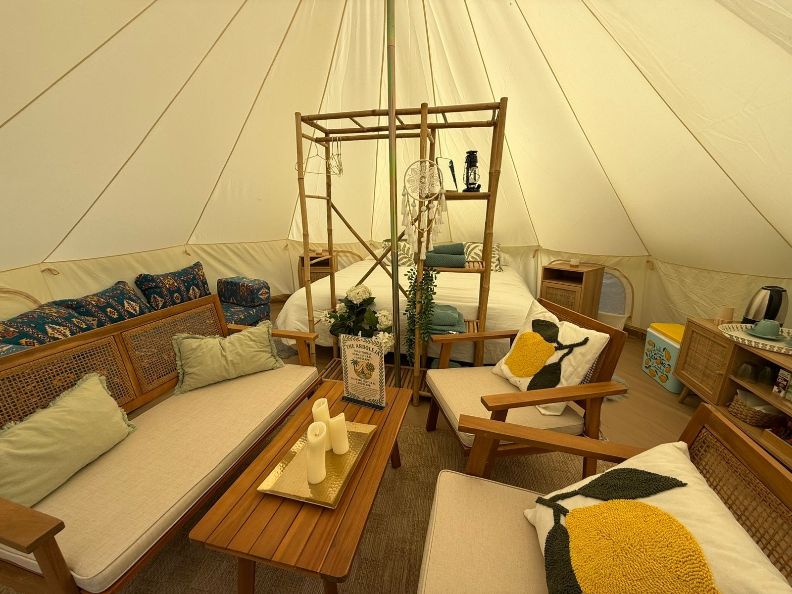 Acogedor interior de tienda glamping con muebles. Sofá y sillas de madera con cojines color limón, cama y estanterías decorativas.