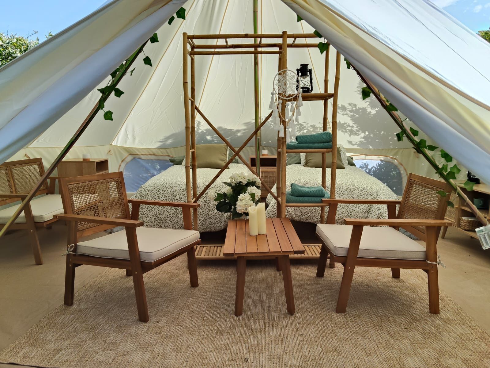 Dentro de una tienda de lona: cama, sillas, mesa y estanterías con toallas y una linterna.