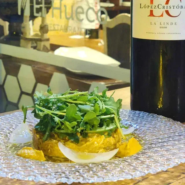 Un plato compuesto con una botella de vino. La comida se sirve en un plato estampado, con verduras y rodeado de cítricos y cebollas.