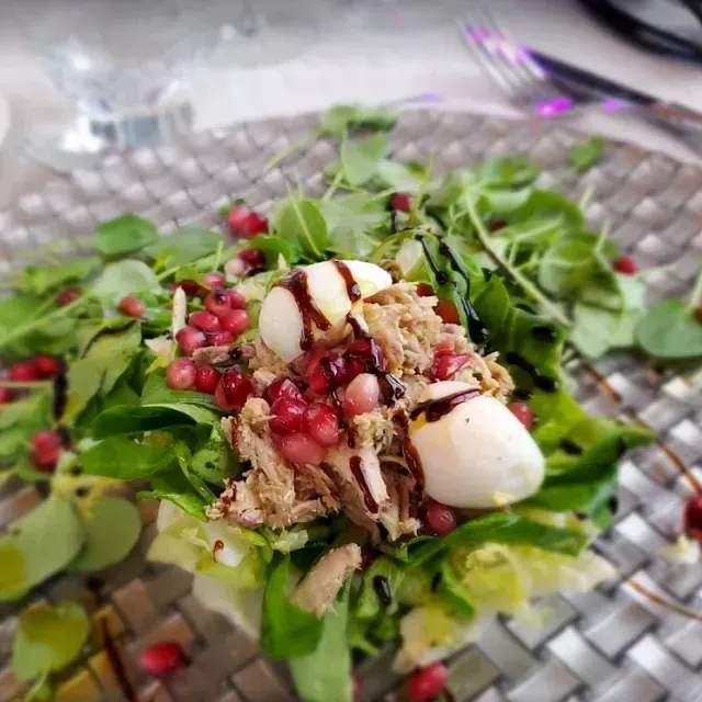Ensalada con rúcula, mozzarella, semillas de granada y carne desmenuzada en un plato de vidrio decorativo.