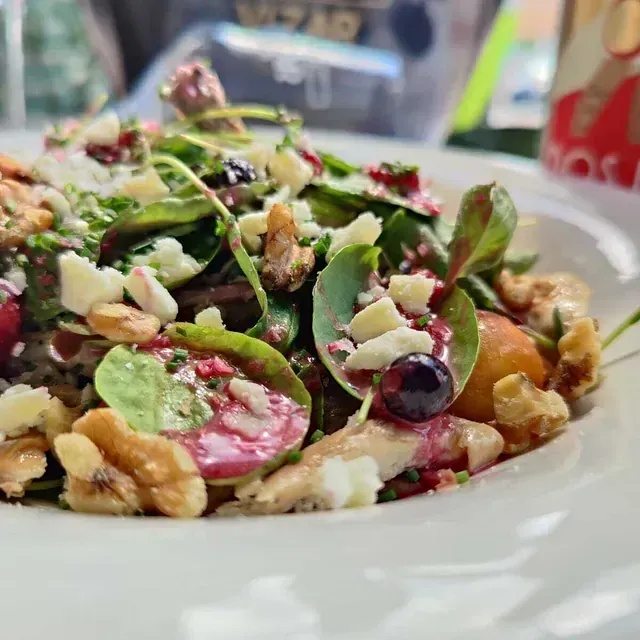 Ensalada con verduras, nueces, bayas y queso en un plato blanco.