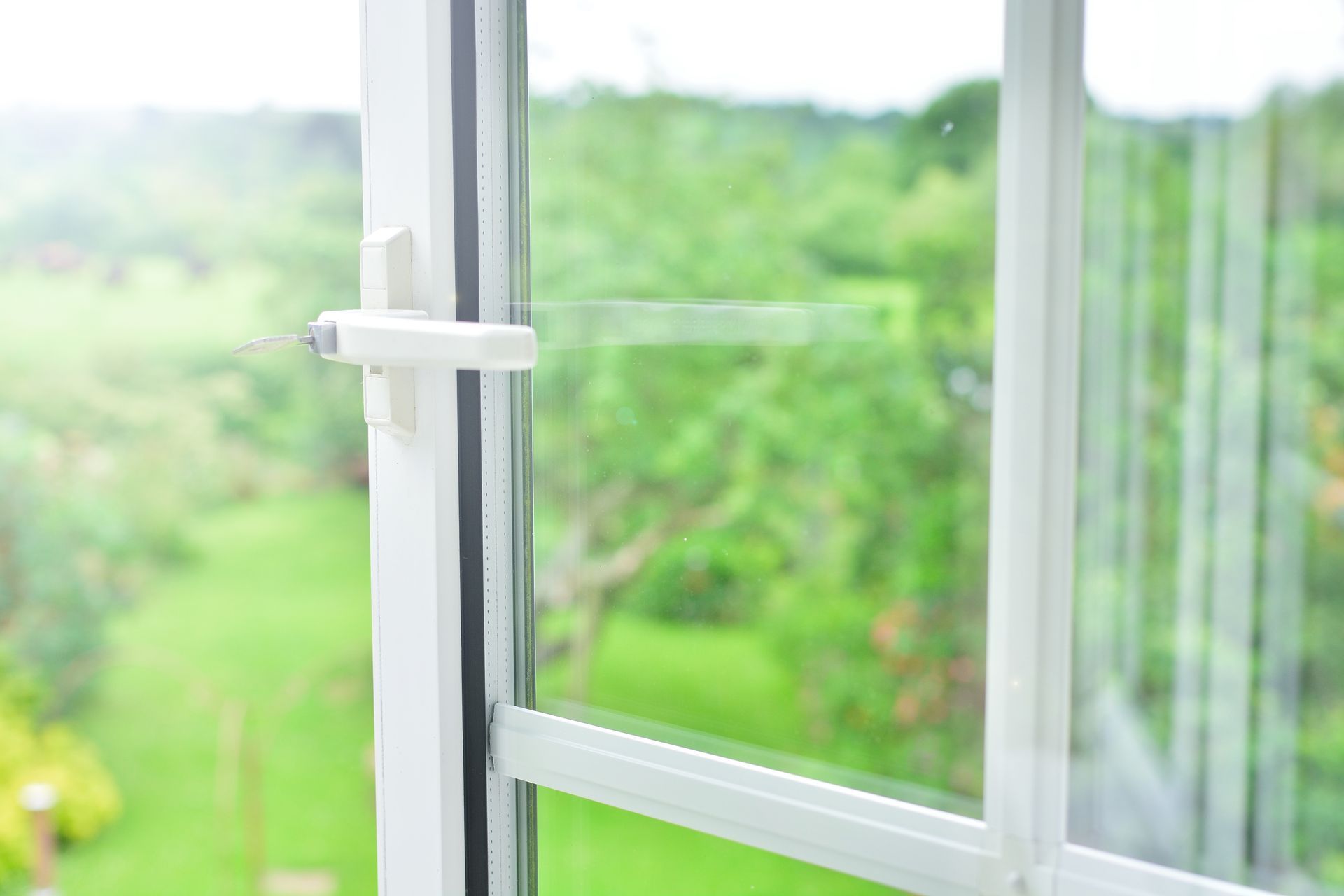 Fenêtre blanche entrouverte. Un câble de sécurité limite l'ouverture. On aperçoit des arbres verts à travers la vitre.