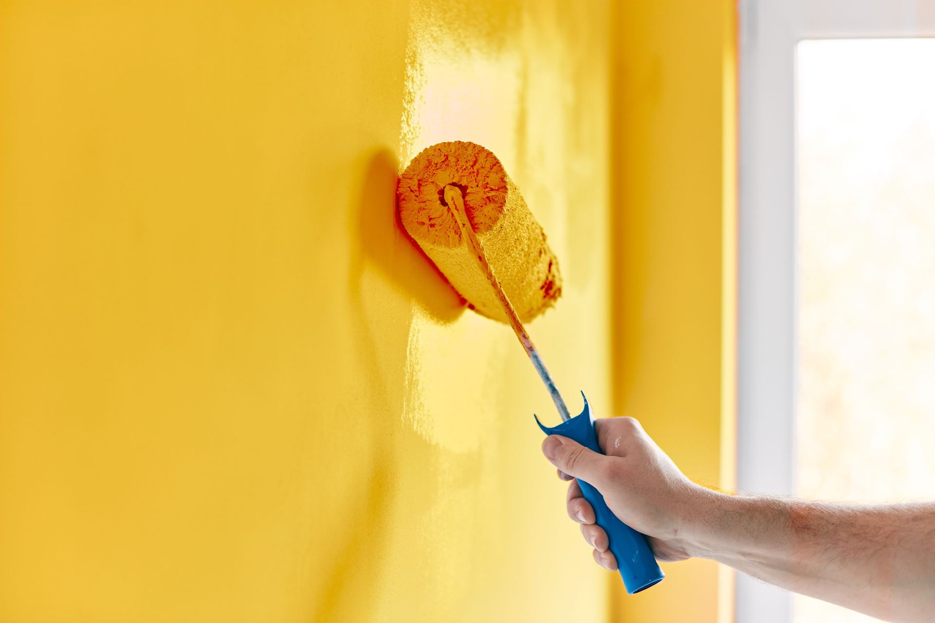 Une personne qui applique de la peinture jaune sur un mur.