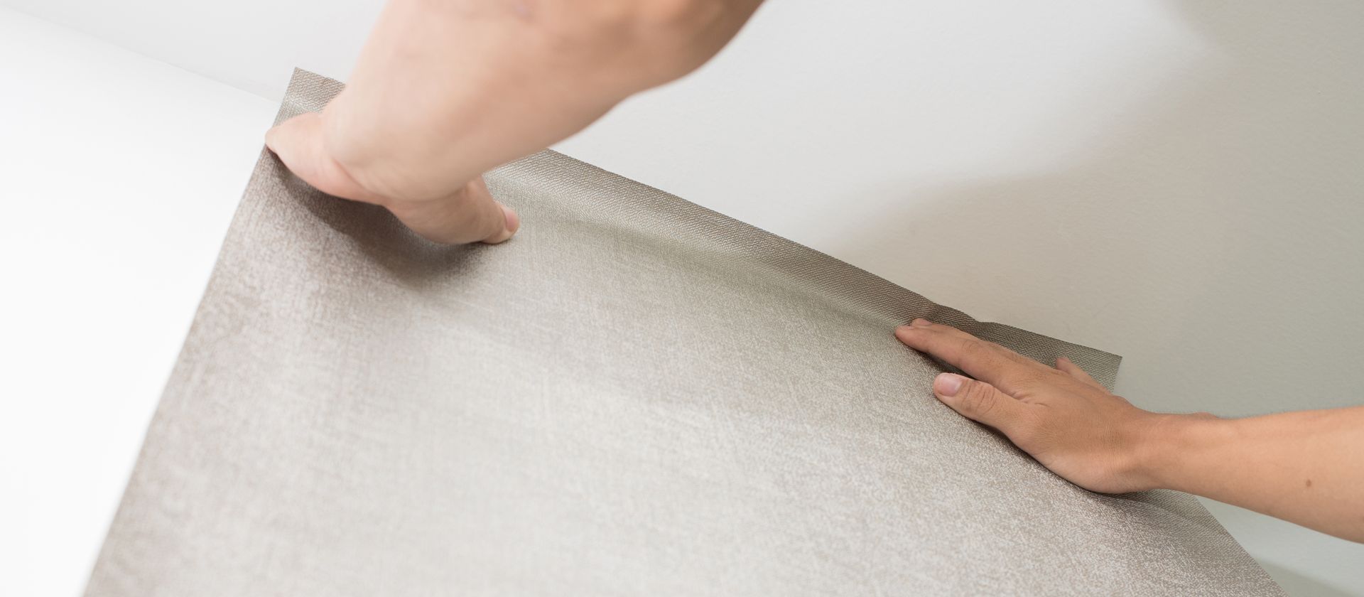 Les mains d'une personne lissant le bord d'un matériau clair sur une surface blanche.